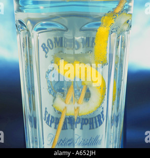 Un verre de gin tonic avec une torsion de citron sur un sucre, et une bouteille de gin Bombay Sapphire derrière. Banque D'Images