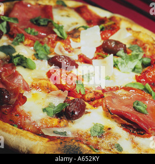 Un home-made, cuite sur pierre pizza garnie de jambon de Parme, mozzarella de bufflonne, olives, tomates italiennes, bébé, copeaux de parmesan et de basilic. Banque D'Images