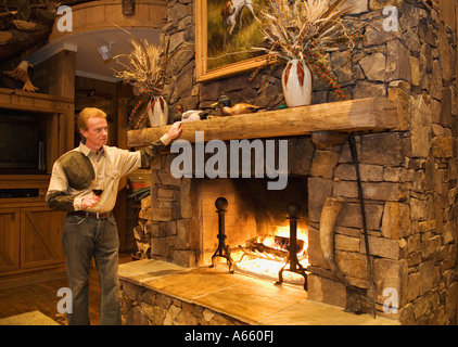 L'homme à côté de détente cheminée dans Lodge avec verre de vin après une journée de chasse de caille Plantation Buckeye Géorgie Banque D'Images