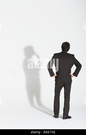 Jeune homme debout, mains sur la hanche, soutenant avec propre ombre, vue arrière Banque D'Images