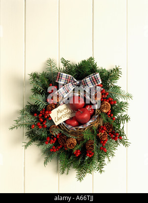 Couronne de fruits rouges et de conifères avec des pommes rouges et ruban tartan sur porte blanche Banque D'Images