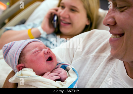 Un heures plus pleurer bébé étant détenu par fier père comme mère répand la bonne nouvelle de l'arrivée du bébé par téléphone. Banque D'Images