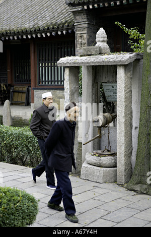 XIAN CHINE hommes musulmans chinois passer devant un ancien puits dans les beaux jardins de la Grande Mosquée de Xi An Banque D'Images