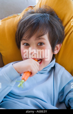 Petit garçon portant sur de gros col roulé de couleur d'or de manger une carotte fraîche oreillers Banque D'Images