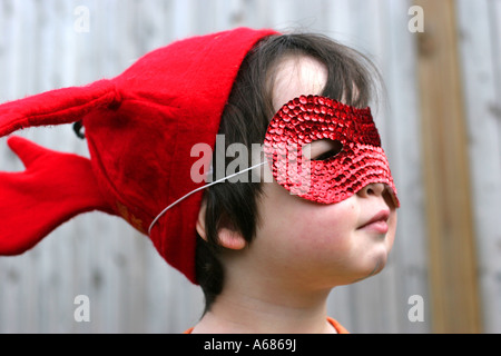 Profil d'un garçon (3-4 ans) portant un masque et un chapeau rouge Banque D'Images