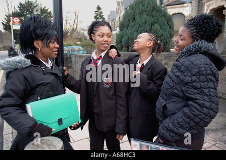 Un groupe de sixième forme les filles à la recherche d'une travail à domicile lors de l'attente à l'arrêt de bus sur le chemin du retour de l'école. Banque D'Images