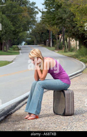 Jeune fille assise sur la valise sur le bord de la route à la triste seul et isolé Banque D'Images