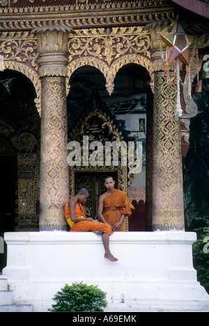 Deux moines novices parler sur le mur de l'entrée wihte d'un temple. Luang Prabang, Laos. Banque D'Images