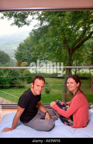 Un couple DANS LA CHAMBRE À COUCHER D'UNE MAISON MODERNE AVEC DES FENÊTRES COULISSANTES UK Banque D'Images