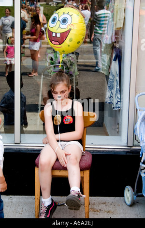 L'âge de 13 ans fille fatigué assis avec des ballons de SpongeBob SquarePants au grand jour foire de rue. St Paul Minnesota USA Banque D'Images