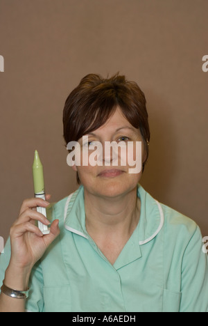 Un audiologiste est titulaire d'une seringue avec un mastic jaune spécial, dans une cabine de son hôpital UK Banque D'Images