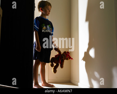 Enfant sortant de la lumière d'un pj et son ours en peluche préféré avoir juste de sortir du lit avec regard inquiet sur son visage Banque D'Images