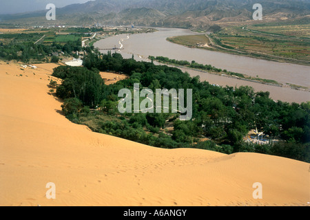 La Chine, Ningxia, Shapotou, fleuve jaune, entre la végétation riveraine d'un côté et à bord d'empiéter sur l'autre face du désert Banque D'Images