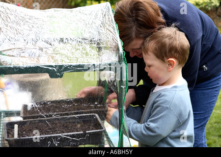 Mère d'aider son jeune fils lieu planté en petits bacs de semences serre plastique pour la germination au début du printemps Banque D'Images