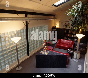 Mur de briques de verre étroit en conversion loft salon avec canapé en cuir rouge et uplighters Banque D'Images