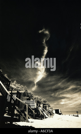 Bien Beach Norfolk. Une vue sur la célèbre des cabines de plage en noir et blanc dans le cadre d'une dramatique, moody sky Banque D'Images