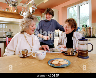 Trois femmes d'ÂGE MOYEN EN Cuisine avec cafetière et de MAGAZINES Banque D'Images