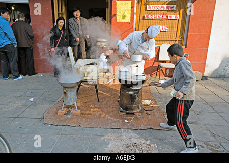 Chine Pékin petit mais occupé restaurant du quartier avec des chefs mis en place sur le trottoir pour préparer le petit déjeuner quenelles Banque D'Images