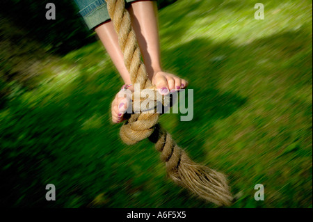 Les pieds d'une fillette de dix ans avec des ongles peints en rouge se balançant sur une corde nouée au-dessus de l'herbe verte en été Banque D'Images