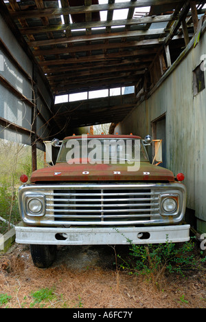 Vieille camionnette Ford de projecteurs stationné sous un vieux hangar usé avec les trous dans le toit vue grand angle Banque D'Images