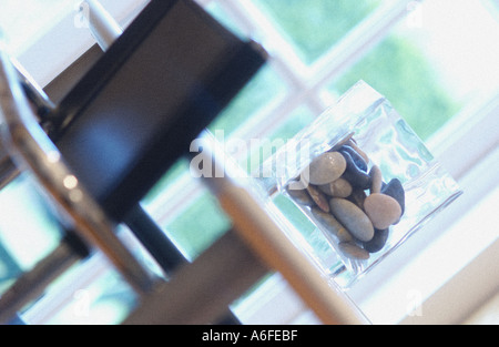 Vase contenant des galets sur une table en verre avec chrome et une chaise en cuir et voir à l'extérieur des fenêtres à la française Banque D'Images