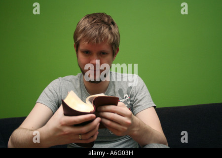 Jeune homme blond lire la Bible avec fond vert lumineux Banque D'Images