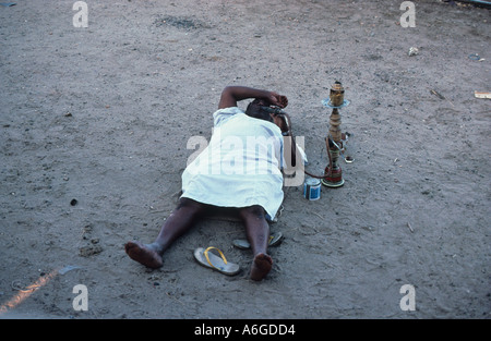 Décontracté homme couché et fumer une pipe narguilé à côté de la ligne de chemin de fer à la gare de Kosti Soudan en raison des pannes des trains c Banque D'Images