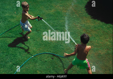 Vue aérienne de deux jeunes garçons ayant une lutte de l'eau dans l'herbe avec deux flexibles Banque D'Images