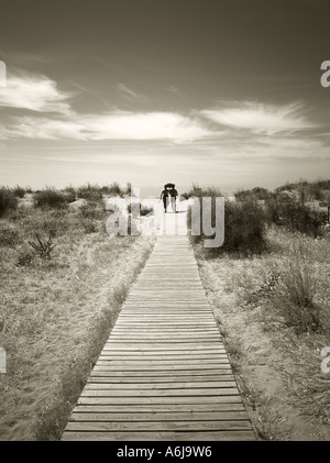 Un couple portant un bébé sur une promenade de bois menant à une vaste plage de sable, à l'extrême Sud Ouest de l'Espagne. Banque D'Images