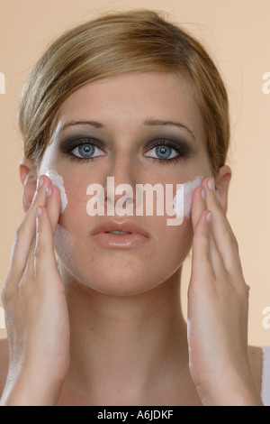 Jeune femme blonde mise sur la crème pour le visage avec les deux mains Banque D'Images