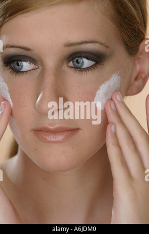 Jeune femme blonde mise sur la crème pour le visage avec les deux mains Banque D'Images