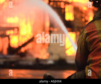 Fire fighter pulvériser de l'eau assis sur burning house Banque D'Images