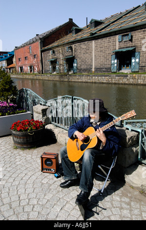 Musicien ambulant qui joue de la guitare dans le passage libre à côté d'un canal historique et des entrepôts à Otaru Japon 2005 Banque D'Images