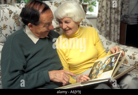 Loving couple sitting on sofa at home à la recherche grâce à l'album photo Banque D'Images