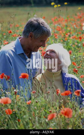Smiling mature woman sitting copule dans champ de coquelicots Banque D'Images