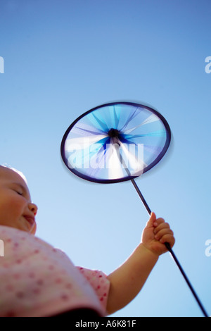 Petit bébé tenant une windwheel dans le ciel Banque D'Images