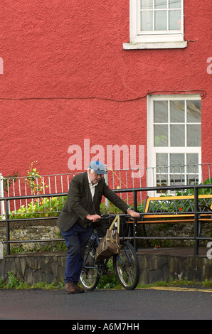 Un vieil homme pousse son vélo en haut d'une colline, à la maison rouge à l'arrière-plan à Kinsale County Cork Irlande Banque D'Images