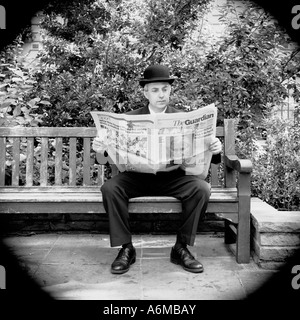 Ville anglaise gent homme d'affaires lisant le journal Guardian assis sur banc dans le parc de Londres Banque D'Images