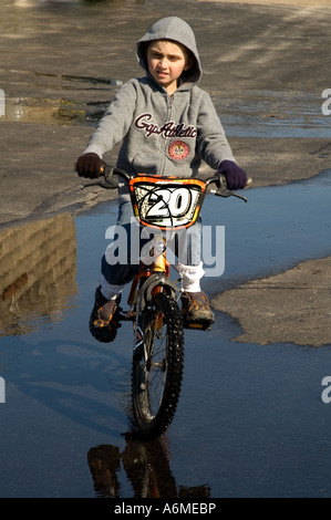 Boy chevauche son vélo à travers les flaques printanières c est la première fois que son vélo a été à l'extérieur depuis l'automne dernier Banque D'Images