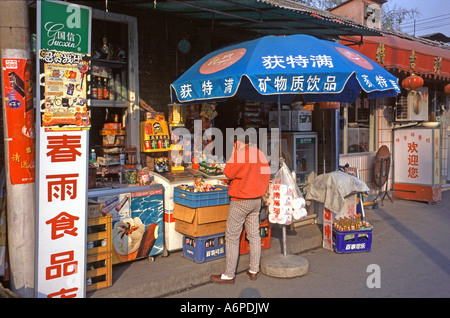 Petite boutique typique dans les rues de Beijing Chine la boutique est un magasin d'alimentation et de l'extérieur est un homme au téléphone Banque D'Images