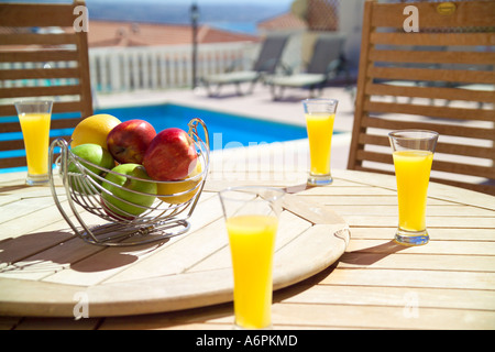 Bol de fruits et les verres de jus d'ORANGE SUR LA TABLE EN BOIS AVEC PISCINE À CHYPRE EN ARRIÈRE-PLAN Banque D'Images