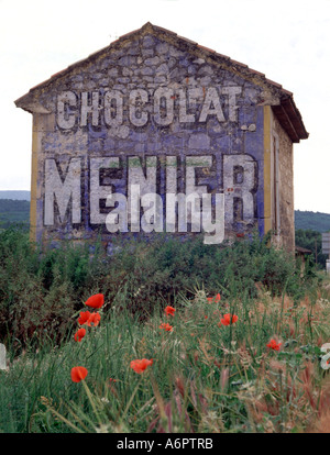 Publicité routière sur une ancienne grange en Provence, Sud de la France. Chocolat Menier avec coquelicots rouges au premier plan. Vieux Sud de la France. Banque D'Images