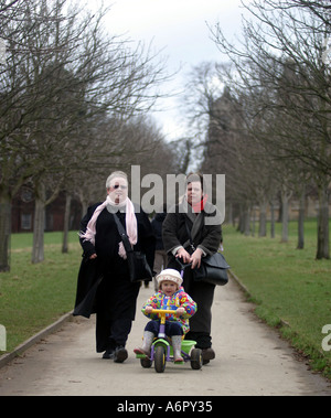 Deux femmes autour d'une petite fille de trois ans sur un tricycle dans Wollaton Park Banque D'Images