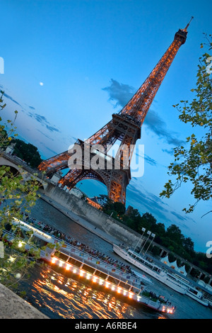 Tour Eiffel bateaux touristiques crépuscule avec des lumières en passant par en Seine en premier plan Paris France Banque D'Images