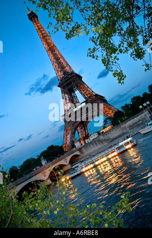 Tour Eiffel bateaux touristiques crépuscule avec des lumières en passant par en Seine en premier plan Paris France Banque D'Images
