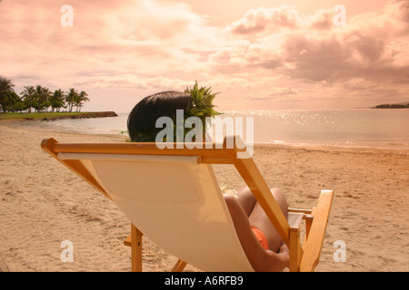 Woman reclining chaise de plage dans le port de haku lei regardant le coucher du soleil sur la plage de sable de Oahu Hawaii Banque D'Images