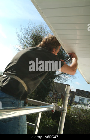 Menuisier travaillant au large de la tour d'échafaudage à la résidence pour plus de clad conseil soffite peint avec un faible niveau de maintenance panneaux plastiques Essex England UK Banque D'Images