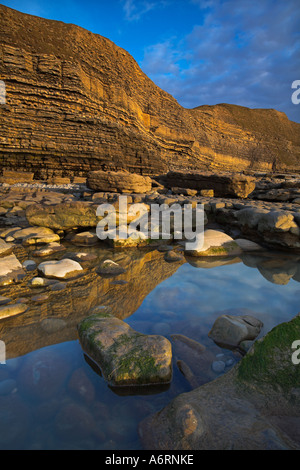 En fin de soirée le soleil baigne les falaises en couches dans une lumière dorée. Cailloux ovale reste sur les bords de la baie de Dunraven, Galles du Sud. Banque D'Images