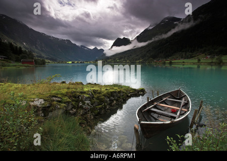Un bateau à rames est intégré en toute sécurité dans les eaux turquoises du lac Olden, tandis qu'un ciel d'orage menaçant au-dessus de la Norvège se bloque Banque D'Images