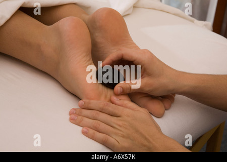 Massothérapeute offrant aux pierres chaudes à la plante des pieds d'une femme. Banque D'Images